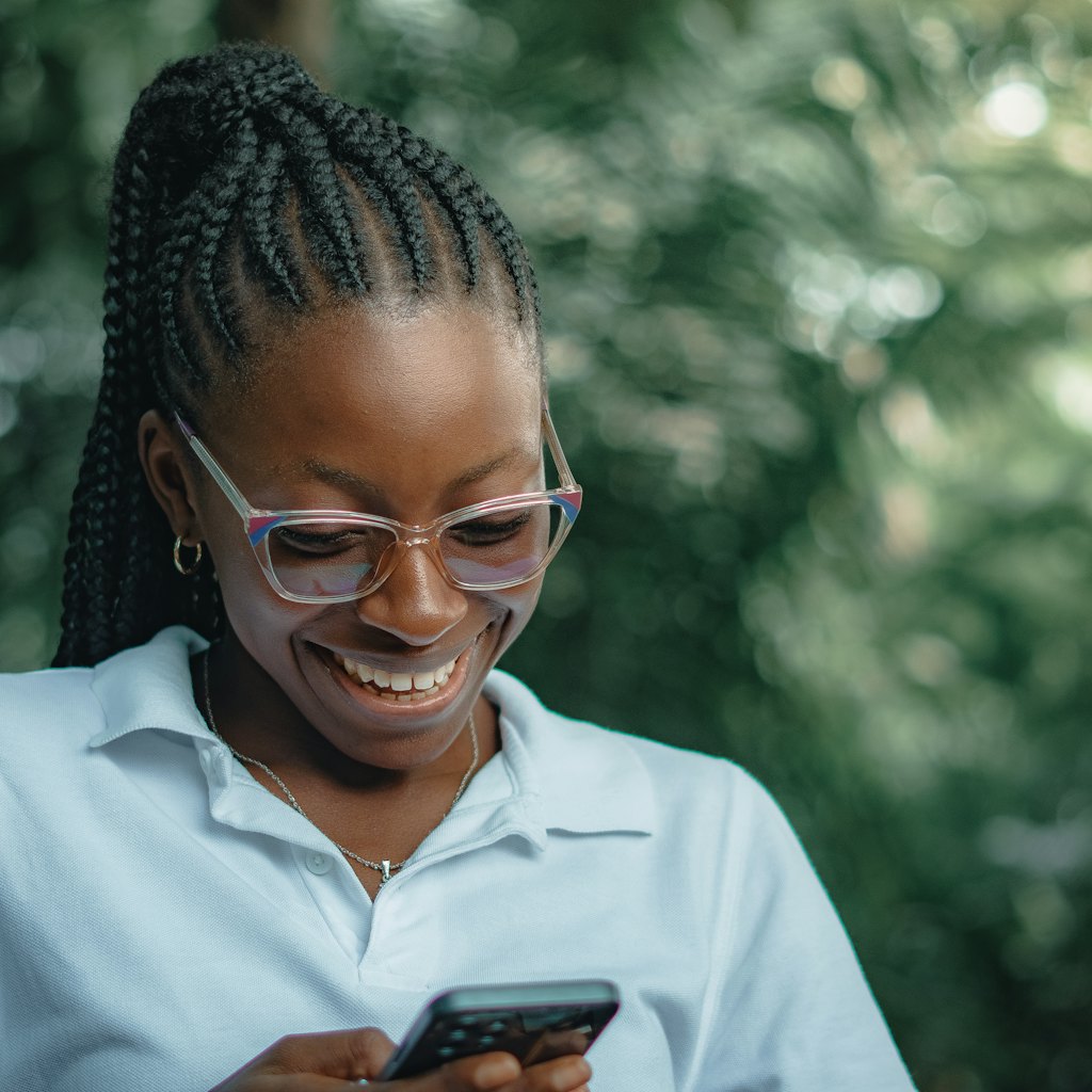 Photo of a smiling woman with glasses looking down at her smartphone