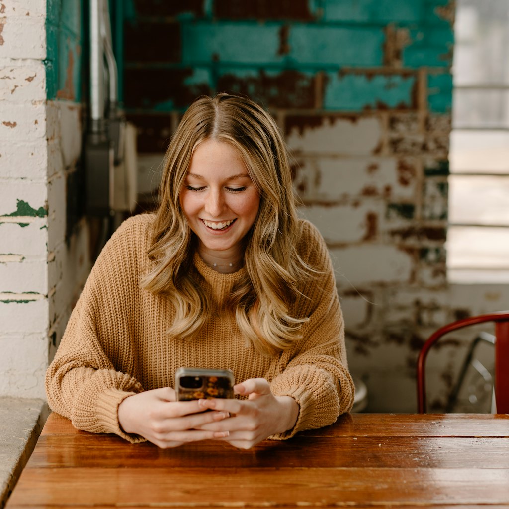 Photo of a woman at a table smiling as she reads the reply on her phone